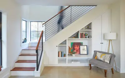 A person ascends a modern staircase, its sleek design contrasting with the built-in bookshelves and storage beneath. This stairwell is a functional art piece.