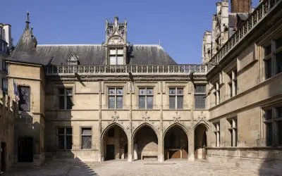 Hof des Musée de Cluny mit gotischer Architektur, Spitzbögen und filigranen Verzierungen unter blauem Himmel.