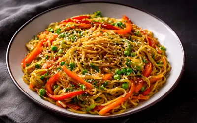 Eine Schüssel mit gebratenen chinesischen Nudeln, garniert mit Erbsen, Paprika und Sesam.