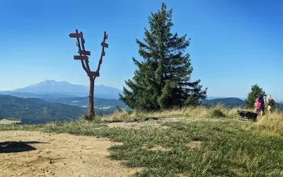 Wysoki wierch z drogowskazem i widokiem na góry. Rodzina z plecakami podziwia panoramę.