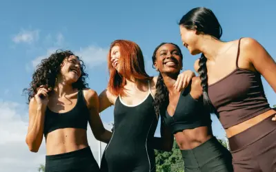 Quatre femmes souriantes, en tenue de sport, profitent du soleil. Leurs abdos sont visibles, suggérant une pratique comme l'abdo hypopressif.