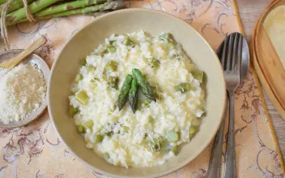 Kremowe risotto ze szparagami, posypane parmezanem, z kilkoma zielonymi szparagami na wierzchu.