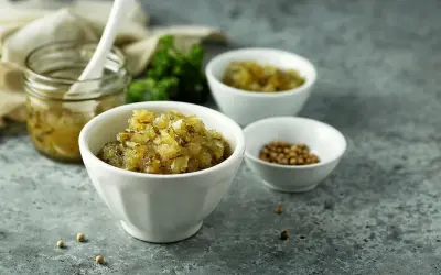 En skål med finhackad bostongurka, perfekt för ditt bostongurka recept. Bredvid en burk med gurka och en skål med senapsfrön.