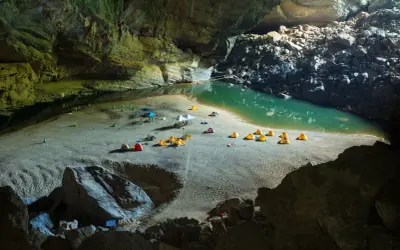 Obóz w jaskini Son Doong: namioty rozbite na piaszczystej plaży nad turkusową wodą, otoczone skalnymi ścianami.