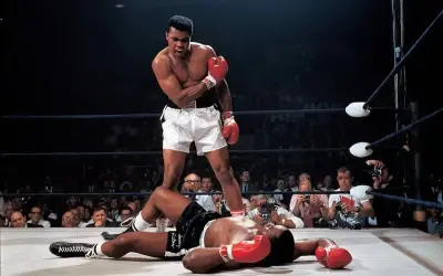 Iconic Muhammad Ali stands over a fallen opponent in the ring, a triumphant roar escaping his lips. A crowd watches, cameras flashing.