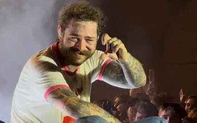 Post Malone na koncercie, uśmiecha się i pokazuje gest ręką.