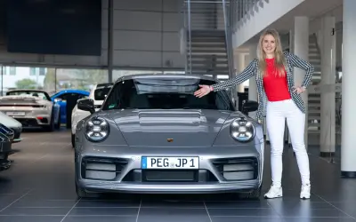 Eine Frau präsentiert stolz einen grauen Porsche Carrera T. Die Wertentwicklung dieses Sportwagens ist ein spannendes Thema für Enthusiasten.