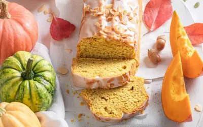 Bizcocho de calabaza Thermomix cubierto de glaseado y almendras. Rodeado de calabazas, hojas de otoño y bellotas.