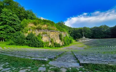 Amfiteatr na Górze Świętej Anny, otoczony zielenią, z kamiennymi ławami i monumentem.