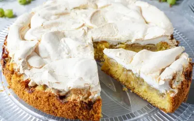 Ein saftiger Stachelbeer Baiser Kuchen mit goldbraunem Boden und fluffiger Baiserhaube, ein Stück davon ist angeschnitten.