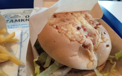 Pyszny burger drwala z chrupiącym bekonem i serem, w papierowym opakowaniu, obok porcji frytek.