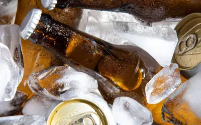 Chłodne piwo w butelkach i puszkach wśród kostek lodu. Szukasz piwa alkoholowego, które ma najmniej kcal?