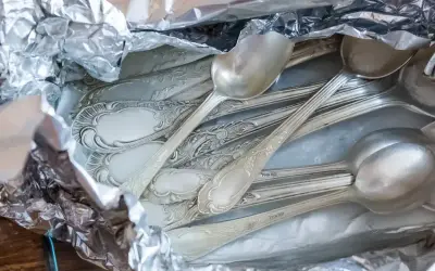 Stare, ozdobne łyżki i widelce owinięte w folię aluminiową, gotowe do czyszczenia srebra.