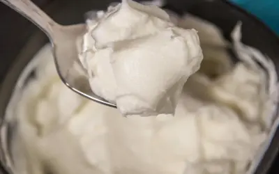 Un cucchiaio raccoglie una generosa porzione di cremoso yogurt greco fatto in casa, pronto per essere gustato.