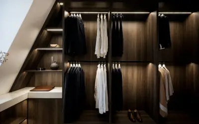 Elegant platsbyggd walk in closet i mörkt trä med stilfull belysning. Hängande kostymer, skjortor och accessoarer.