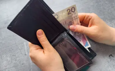 Ręce wkładają banknot 20 zł do portfela. Dowiedz się, komu przysługuje zasiłek dla bezrobotnych.