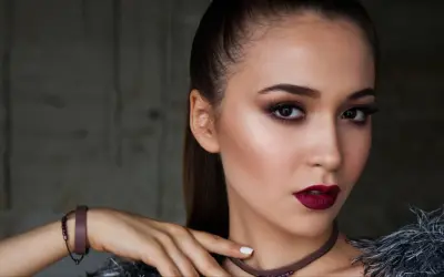 Kobieta z wyrazistym makijażem wieczorowym, ciemnymi ustami i smoky eyes. Długie włosy spięte w kucyk.