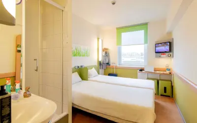 Pokój w hotelu Ibis z dwoma łóżkami, łazienką, biurkiem z laptopem i telewizorem.