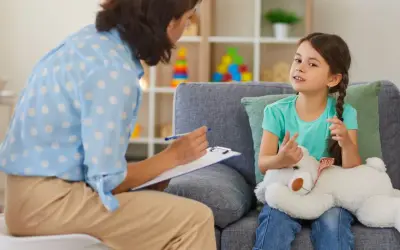 Psychoterapeutka z notatkami rozmawia z dziewczynką trzymającą misia.
