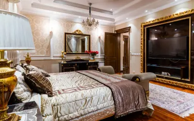 Elegancka sypialnia glamour beżowa z bogato zdobionym łóżkiem, kryształowym żyrandolem i złotymi detalami.