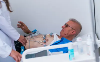 Mężczyzna z elektrodami EKG na klatce piersiowej, pod opieką lekarzy, w stanie przedzawałowym.