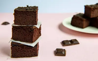 Ciemne, wilgotne brownie z fasoli, ułożone w stosik, obok kawałków czekolady.