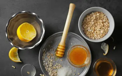 Zutaten für ein natürliches Peeling zur Hautentgiftung: Haferflocken, Honig, Zitrone und Zucker.