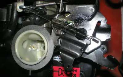 Mechanizm kosiarki z widoczną linką gazu, sprężynami i elementami gaźnika.
