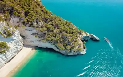 Piękna plaża i turkusowe morze, idealne miejsce, by zastanowić się, gdzie do Włoch na wakacje. Statek wycieczkowy zbliża się do skalistego wybrzeża.