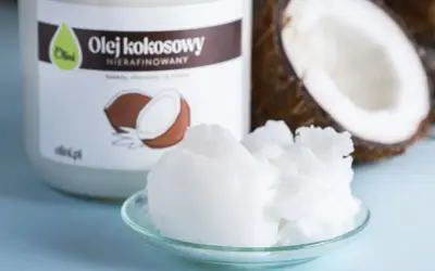 Olej kokosowy nierafinowany na talerzyku, obok słoika i połówki kokosa. Idealny do smażenia i pieczenia.
