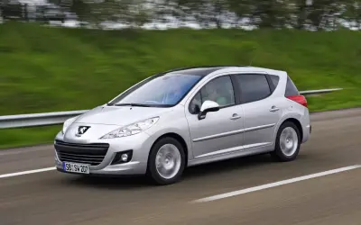Srebrny Peugeot 207 1.6 HDI z czarnym dachem pędzi po drodze, za kierownicą siedzi mężczyzna, a obok niego pasażerka.