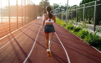 Kobieta w sportowym stroju biegnie po bieżni w słoneczny dzień.