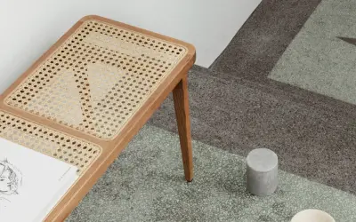 En bänk med rottingdetaljer står på ett terazzogolv. Rottingen är ett naturligt material som kan se ut som om det är på väg att ruttna om det inte sköts rätt.