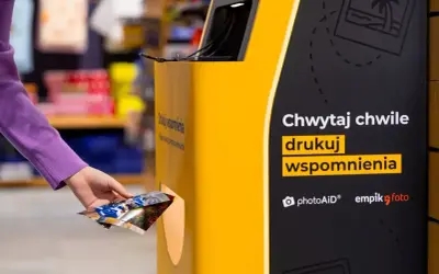 Ręka wyjmuje wydrukowane zdjęcia z automatu. Teraz wiesz, jak wywołać zdjęcia w Empiku i drukować wspomnienia.