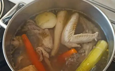 Gotowanie rosołu bez przykrycia. W garnku bulgoczą kawałki kurczaka, marchewka, por i inne warzywa.