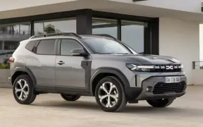 Szary Dacia Duster, jeden z najlepszych aut do gazu, parkuje przed nowoczesnym budynkiem.