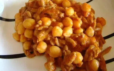 Un plato de garbanzos con carne picada, cocinado en una salsa rojiza y servido en una vajilla blanca con rayas negras.