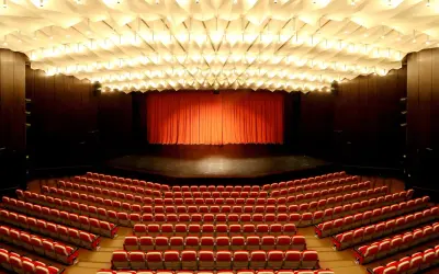Leere rote Sitze im **Theater und Konzerthaus Solingen** warten auf Besucher. Die Bühne ist mit einem roten Vorhang verdeckt.
