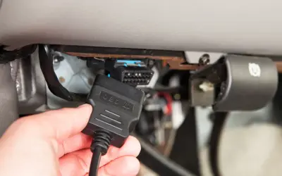 Ręka podłącza kabel OBD II do złącza diagnostycznego pojazdu, aby sprawdzić błędy DTC.