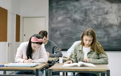 Uczniowie skupieni na zadaniach. Dziewczyna pisze, druga czyta. W tle tablica. Kiedy skończą, będą wiedzieć, jak budowa future perfect simple.