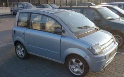 Niebieski, miejski samochód, który może być idealnym pierwszym autem od 16 lat. Stoi na parkingu obok innych pojazdów.