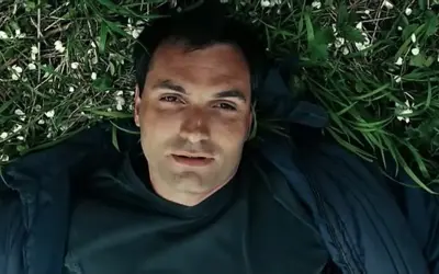 Mężczyzna leży na trawie, otoczony zielenią i białymi kwiatkami. Może to scena z filmu, gdzie wino truskawkowe obsada odgrywa ważną rolę.