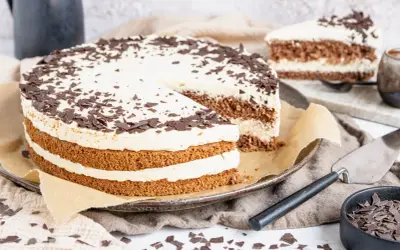 Eine köstliche Cappuccino Torte mit Schokoladenraspeln bestreut, auf einem Teller mit einem angeschnittenen Stück.