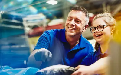 Un uomo e una donna sorridono mentre lavorano insieme. Un esempio di inclusione e pari opportunità, anche per le ferie categorie protette.