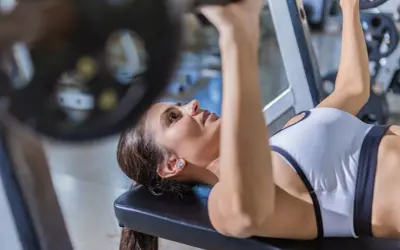 Kvinna utför incline press med skivstång på ett gym.