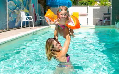 Mamma solleva la figlia con braccioli arancioni in una piscina, un momento di gioia in un bagno giardino a Cesenatico.