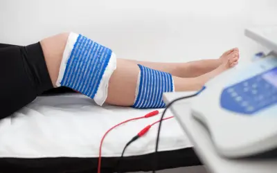 Elektrody podłączone do urządzenia rehabilitacyjnego przy nodze, gdzie widoczna jest kość piszczelowa.