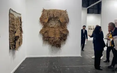 Exhibición de arte contemporáneo con tapices texturizados y personas observando.