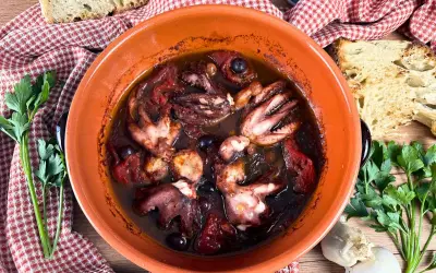 Polipetti alla luciana in terracotta, con pomodoro, olive e pane tostato.