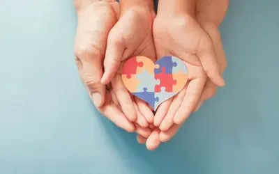 Dłonie trzymają serce z puzzli, symbolizujące wsparcie dla osób z autyzmem i ich unikalne wokalizacje.